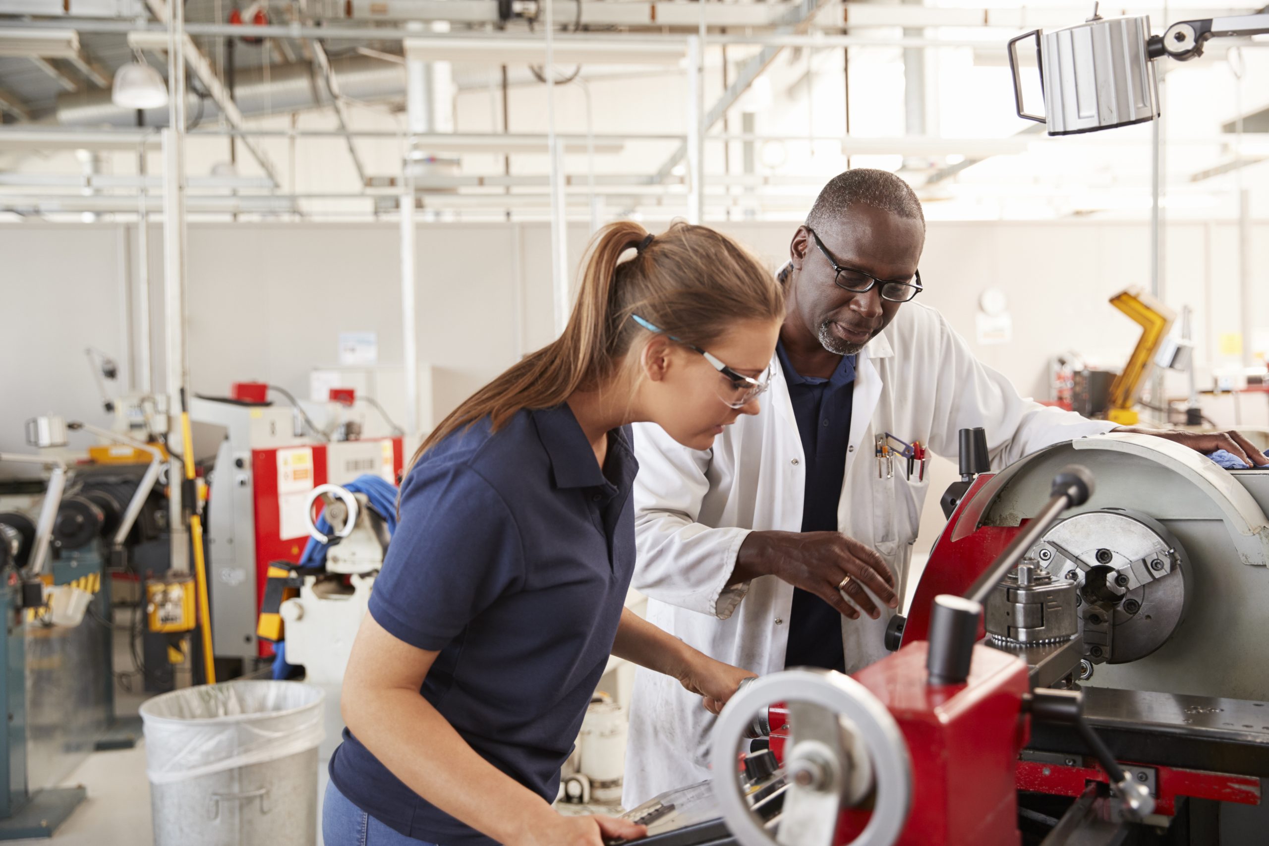 An engineer showing an apprentice how to operate a machine