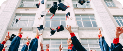 Graduation ceremony with a zoomed in view of students arms throwing blue caps with orange tassels into the air